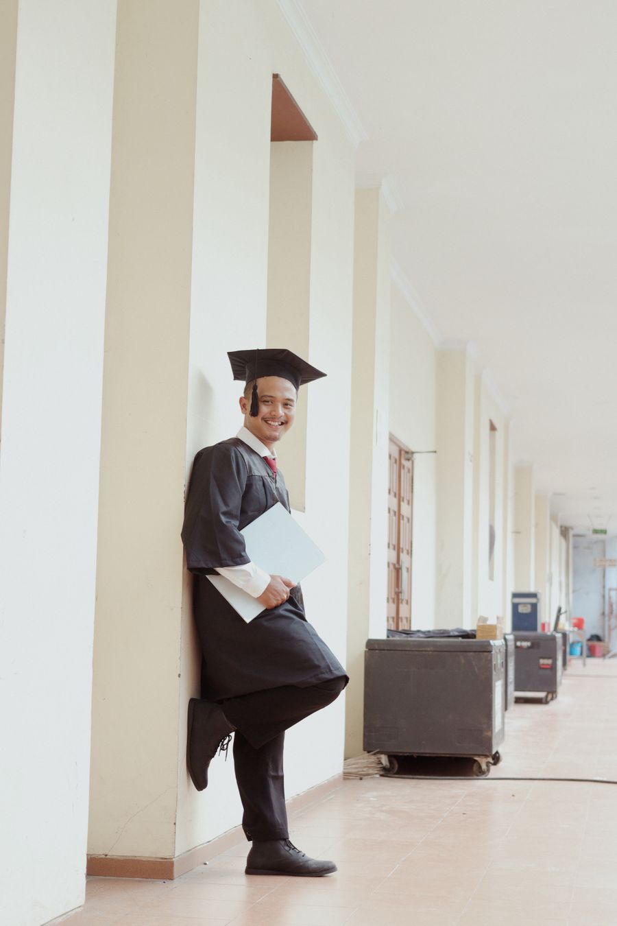 A graduate standing confidently in a campus corridor