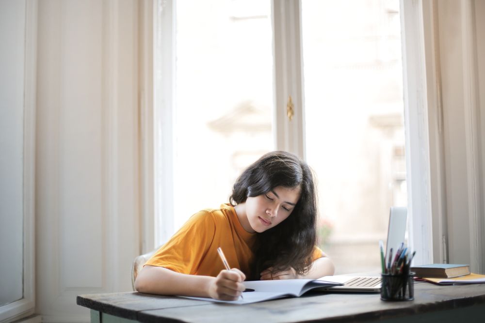 A woman writing an essay by a window